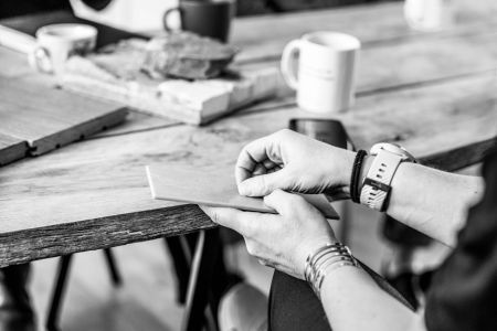 Närbild på händer som undersöker ett materialprov vid ett bord med kaffekoppar och andra prover – fokus på materialval och taktil känsla.