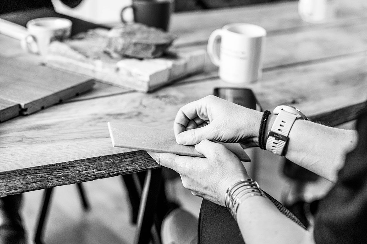 Närbild på händer som håller i ett materialprov vid ett bord, med kaffekoppar och andra prover i bakgrunden.