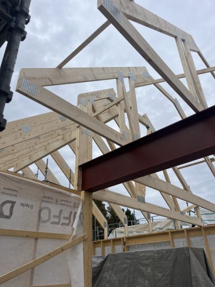Byggarbetsplats med synlig takkonstruktion i trä och stålbalk, under uppförande mot en mulen himmel – fokus på stomme och konstruktion.
