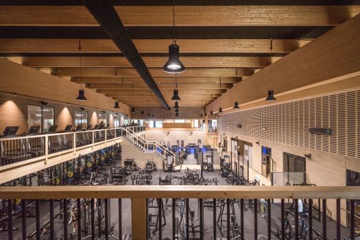 Stort gym i träkonstruktion med öppen planlösning, fria vikter och träningsmaskiner på två våningsplan.