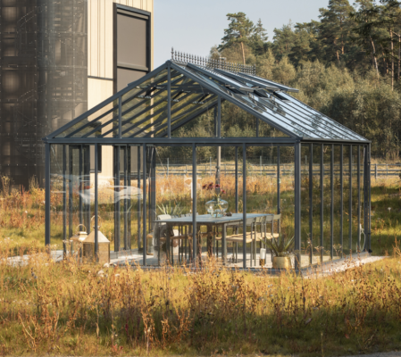 Glashus eller växthus i metallstruktur placerat i ett öppet gräslandskap, inrett med matbord och stolar – modern utemiljö med naturkontakt.