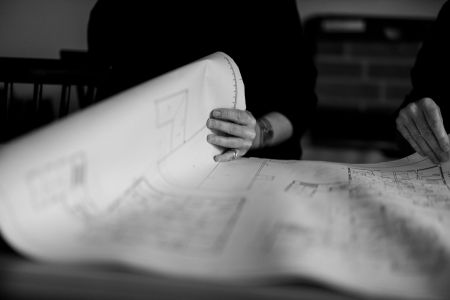 Två personer granskar en stor pappersritning i svartvitt – fokus på arkitekturplanering och byggdokumentation.